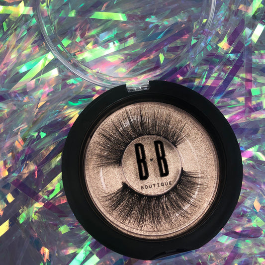 Another photo of Foxy lash with hard plastic container fully opened showing the eyelashes. B heart B logo in the center of packaging. Lashes laying in a holographic background.