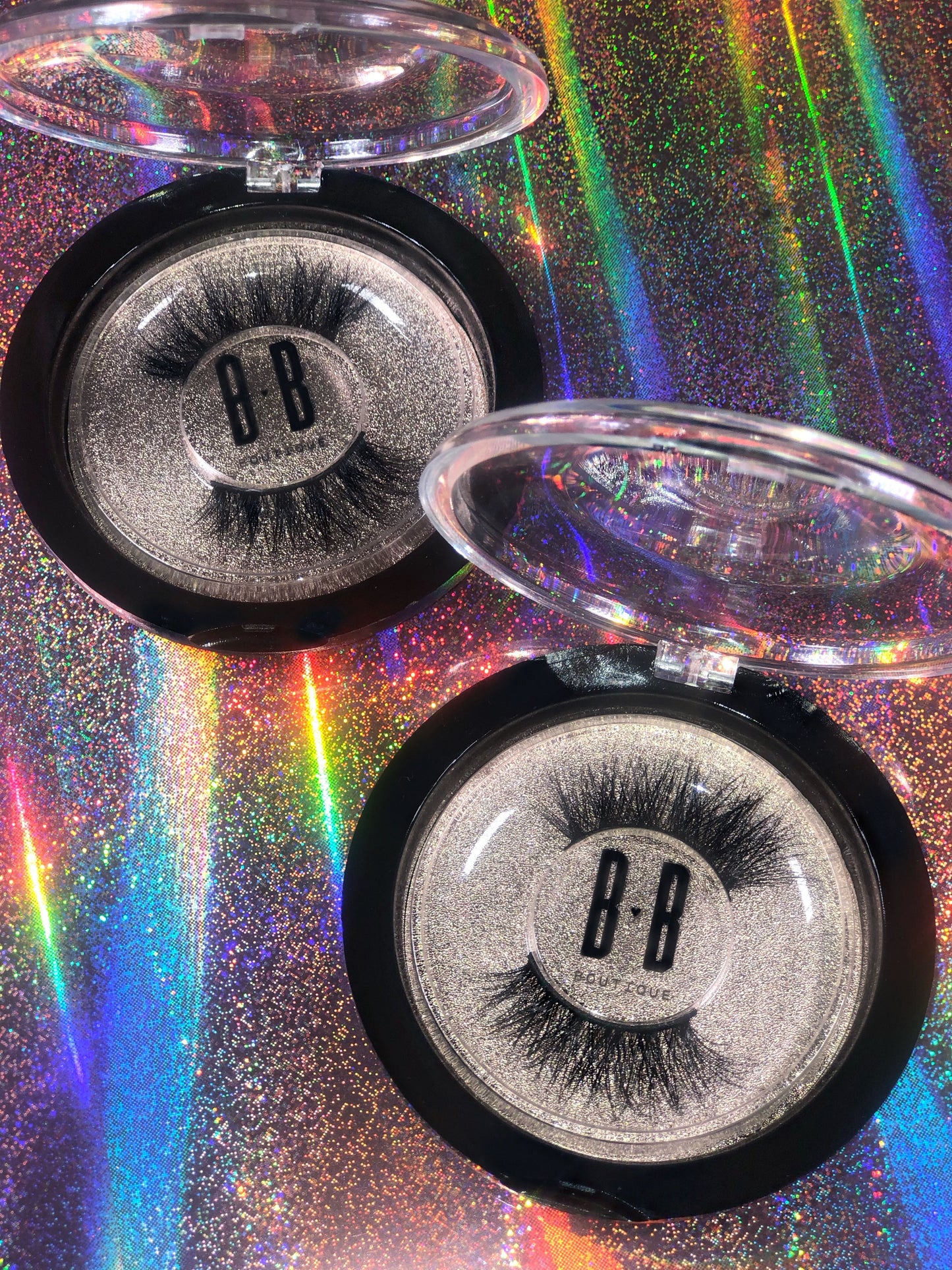 Rainbow holographic background with two pairs of lashes inside hard plastic containers opened showing 3/4 lash band in style Flirty.